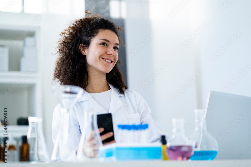 Smiling female scientist with smart phone looking away in hospital Smiling female scientist with smart phone looking away in hospital