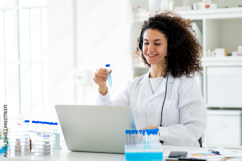Smiling female researcher with test tube working on laptop at clinic Smiling female researcher with test tube working on laptop at clinic