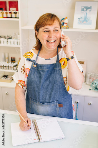 Smiling mature woman taking order over phone in cake shop