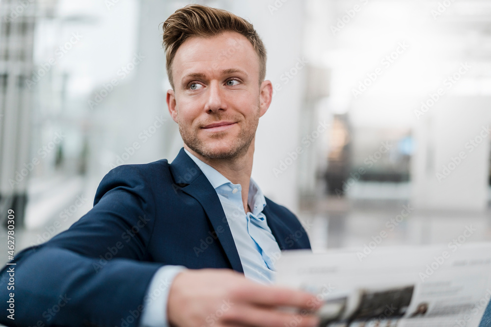 Smiling businessman with newspaper looking away while sitting in city Smiling businessman with newspaper looking away while sitting in city
