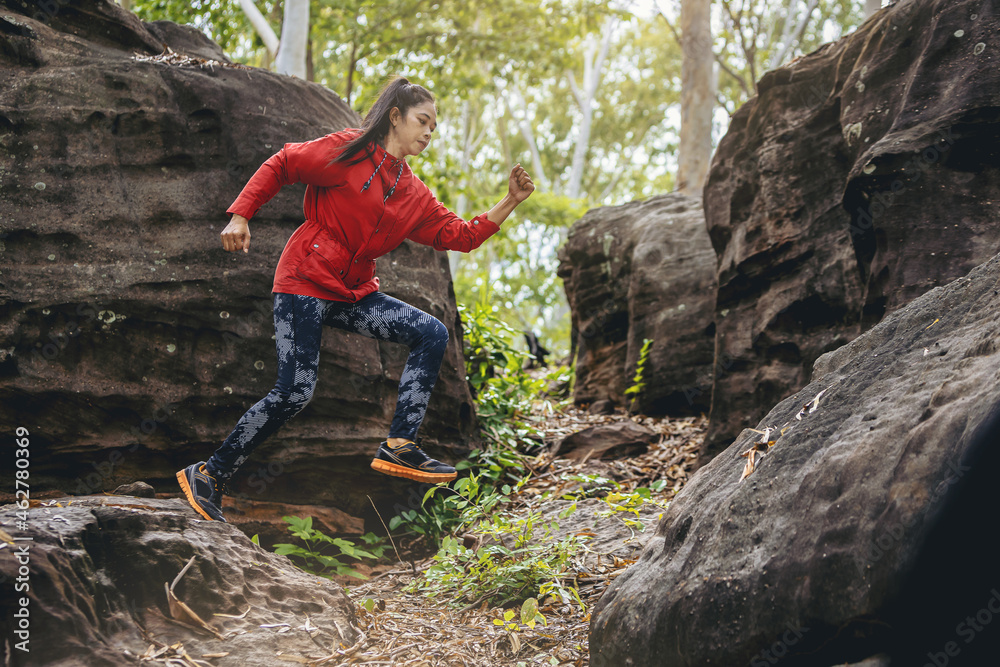 Naklejka premium Sport running woman in cross country trail run jumping on the rocky mountain path. 