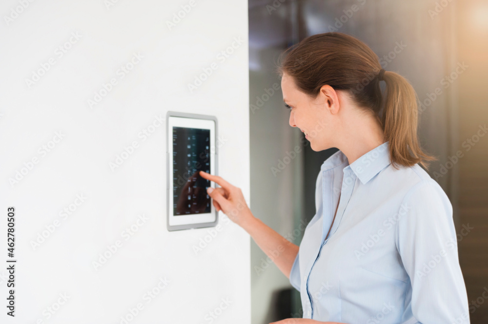 Mid adult woman using digital lightning control on wall at home Mid adult woman using digital lightning control on wall at home