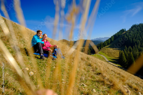 Germany, Bavaria, Hoernle near Bad Kohlgrub, happy young couple having a break sitting in meadow in alpine landscape photo