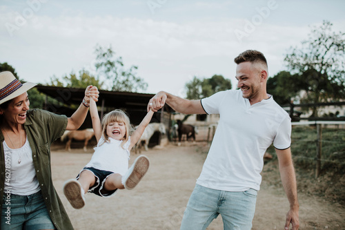 Playful parents holding daughter's hands and swinging her while standing on land