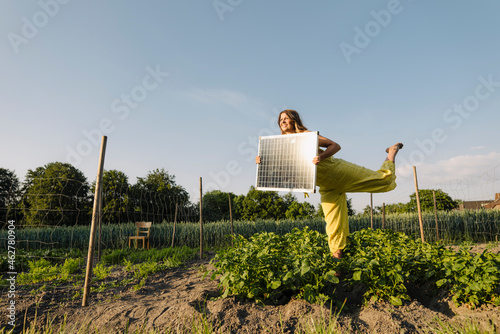 Young woman standing in a vegetable patch in the countryside holding solar panel photo
