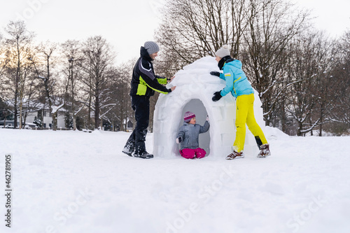 Father and mother helping daughter to build igloo in snow at park