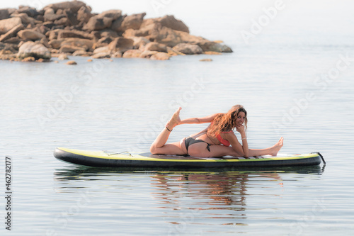 Smiling flexible woman practicing yoga on paddleboard photo