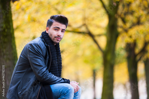 Handsome young man sitting at park during autumn photo