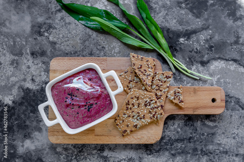 Cutting board, bowl of beetroot dip, crispbread and fresh ramson photo