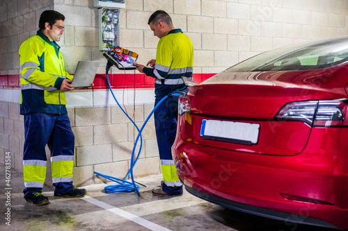 Male technicians working by meter while charging electric car in auto repair shop photo