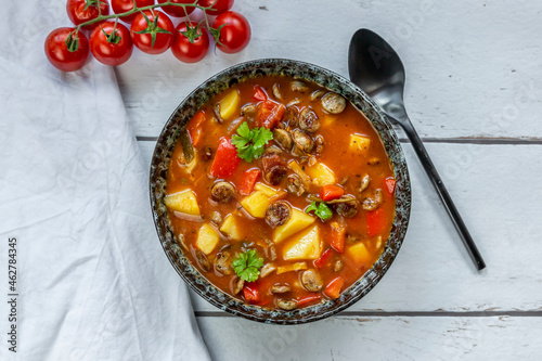 Bowl of sausage goulash with potatoes, tomatoes, bell peppers, leek and parsley photo
