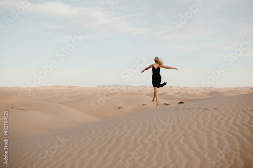 Back view of blond woman jumping in the air, Algodones Dunes, Brawley, USA photo