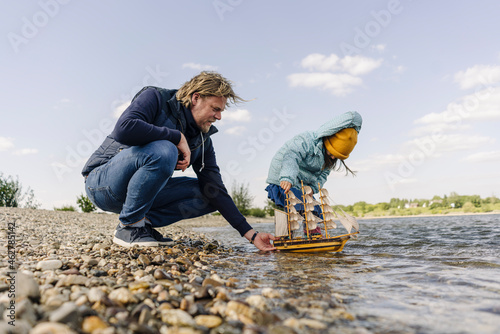 Father and daughter playing with toy boat near bank river photo