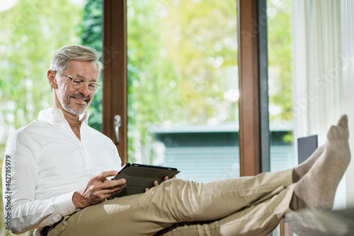 Smiling senior man with grey hair in modern design living room sitting on couch using photo