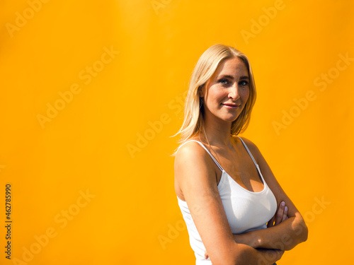 Attractive woman with arms crossed standing against yellow wall photo