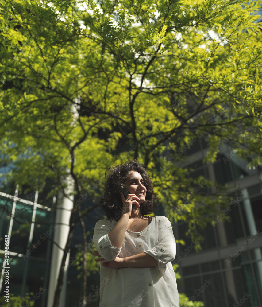 Smiling young woman talking on mobile phone while standing against tree Smiling young woman talking on mobile phone while standing against tree