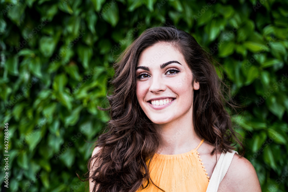 Smiling beautiful young woman with long brown hair standing against plants Smiling beautiful young woman with long brown hair standing against plants