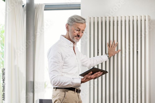 Senior man with grey hair in modern design living room holding tablet checking his smarthome heating