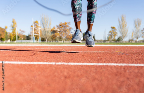 Female athlete jumping with jump rope over sports track on sunny day photo