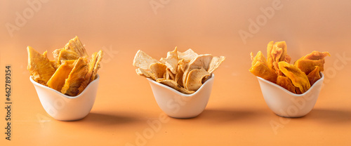 Different dried fruit slices, mango, pineapple, apple into white bowls at beige background. Healthy snack for modern diet.