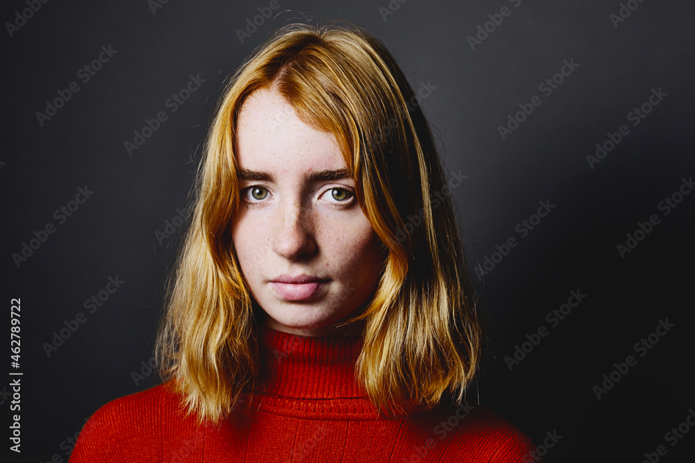 Blond teenage girl staring while standing against gray background