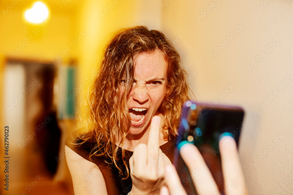 © JAN TEPASS/Westend61 - Close-up of aggressive woman showing middle finger on video call over smart phone at home © JAN TEPASS/Westend61 - Close-up of aggressive woman showing middle finger on video call over smart phone at home