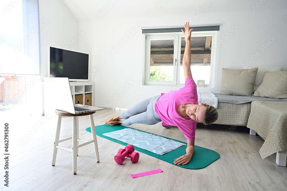 Mature woman with laptop practicing yoga on gym mat in living room Mature woman with laptop practicing yoga on gym mat in living room
