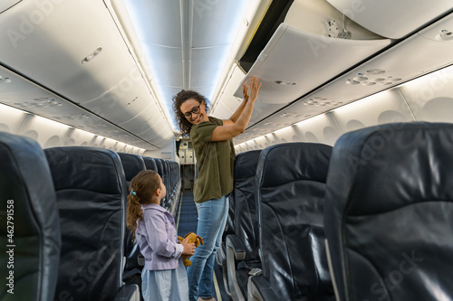 Happy woman folding luggage and looking at her daughter on the plane. Travel and family concept