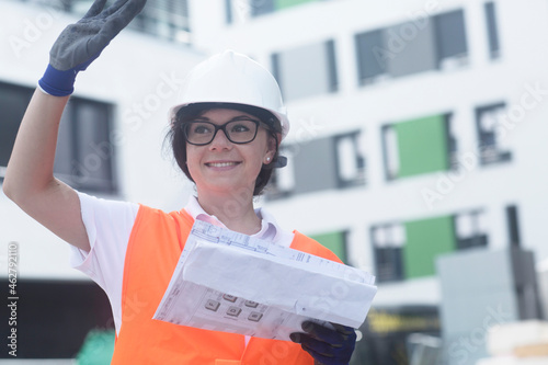 Female construction engineer with construction plan, waving
