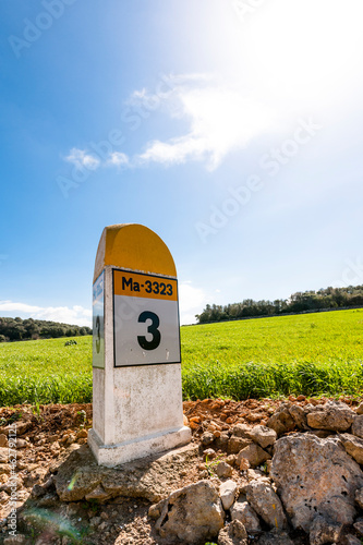 Sun shining over distance marker placed on edge of countryside meadow