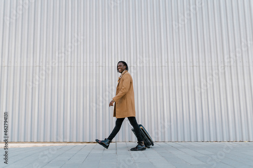 Smiling man walking with suitcase against gray wall