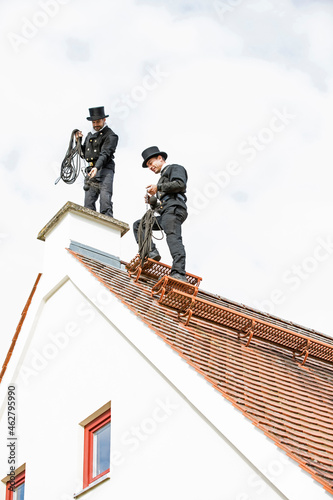Two chimney sweeps working on house roof