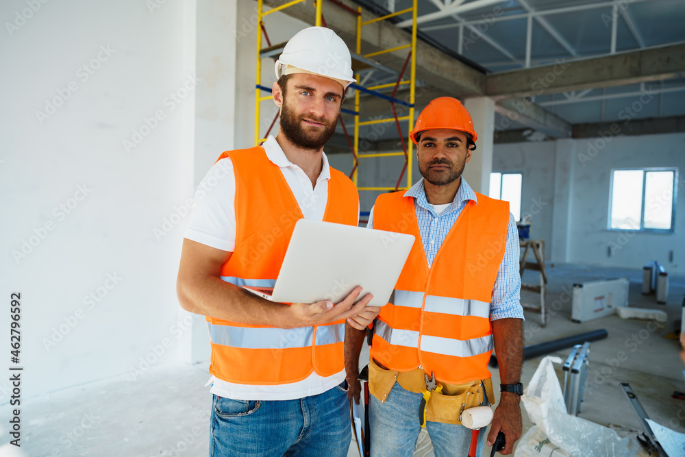 Two specialists supervisors in hardhats using laptop at construction site for work Two specialists supervisors in hardhats using laptop at construction site for work