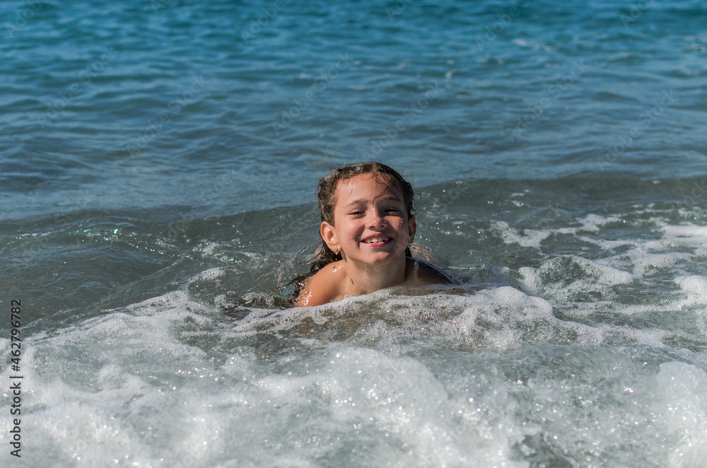 Little happy adorable girl child swims in the sea and plays on the waves during the holidays on the sea coast	
