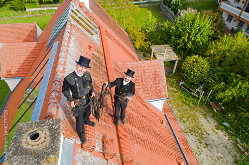 Portrait of two smiling chimney sweeps standing on house roof photo