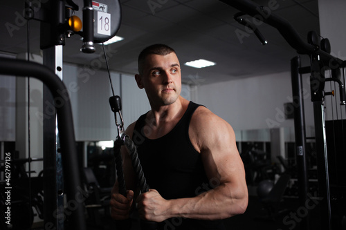 A sports athlete coach a muscular man does an exercise on a simulator in gym. Portrait, low key, darkness. builds up arm muscles