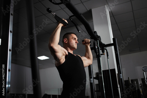 Portrait of an athlete, a sports man coach does an exercise on simulator in the gym. Healthy active lifestyle, shakes muscles. sexual