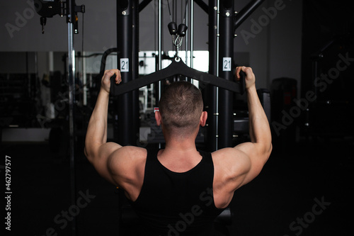 portrait of a handsome male coach in gym. The athlete does an exercise on the simulator in the gym. Builds muscle, plays sports, a healthy lifestyle. rear view