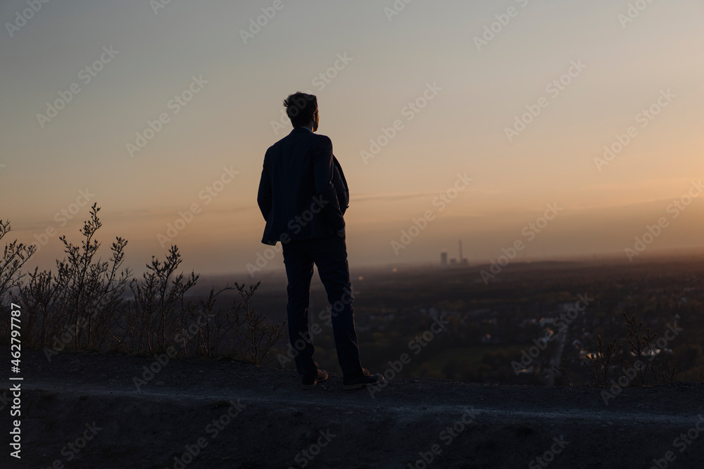Mature businessman standing on a disused mine tip at sunset looking at view Mature businessman standing on a disused mine tip at sunset looking at view
