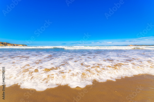 Sea waves rushing towards shore at beach against blue sky in Otago, South Island, New Zealand