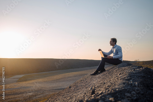 Mature businessman using laptop on a disused mine tip at sunset photo