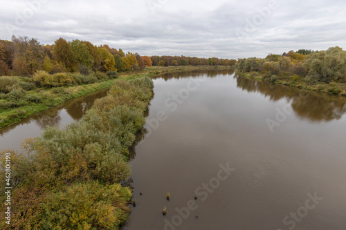 Autumn landscape with a river. Cloudy autumn day by the river. View of the river with trees and bushes on the bank. Bright colors of autumn on a cloudy day.