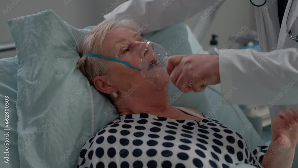 Sick patient breathing heavily while doctor giving help with oxygen mask for respiratory problem. Medic and nurse helping senior woman with medical equipment for healthcare and recovery.