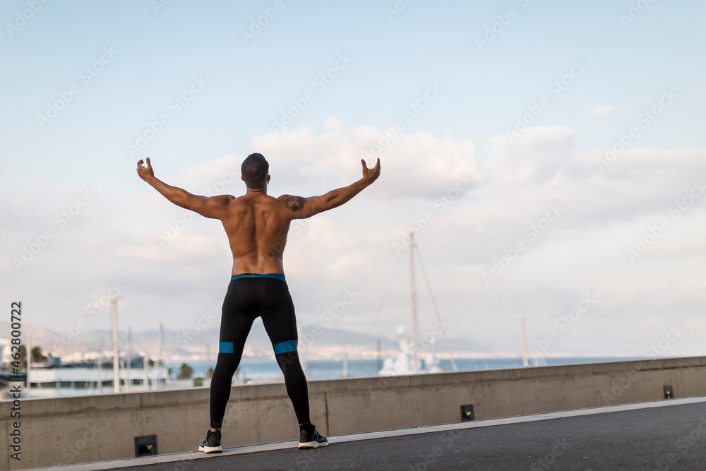 Rear view of a jogger raising arms during workout at the harbour, Barcelona, Spain Rear view of a jogger raising arms during workout at the harbour, Barcelona, Spain