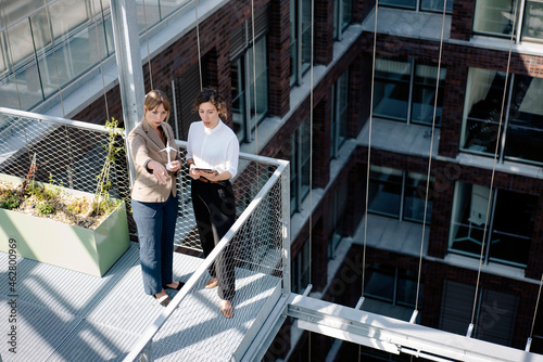 Two businesswomen with tablet and wind turbine model having a meeting on balcony of an office building