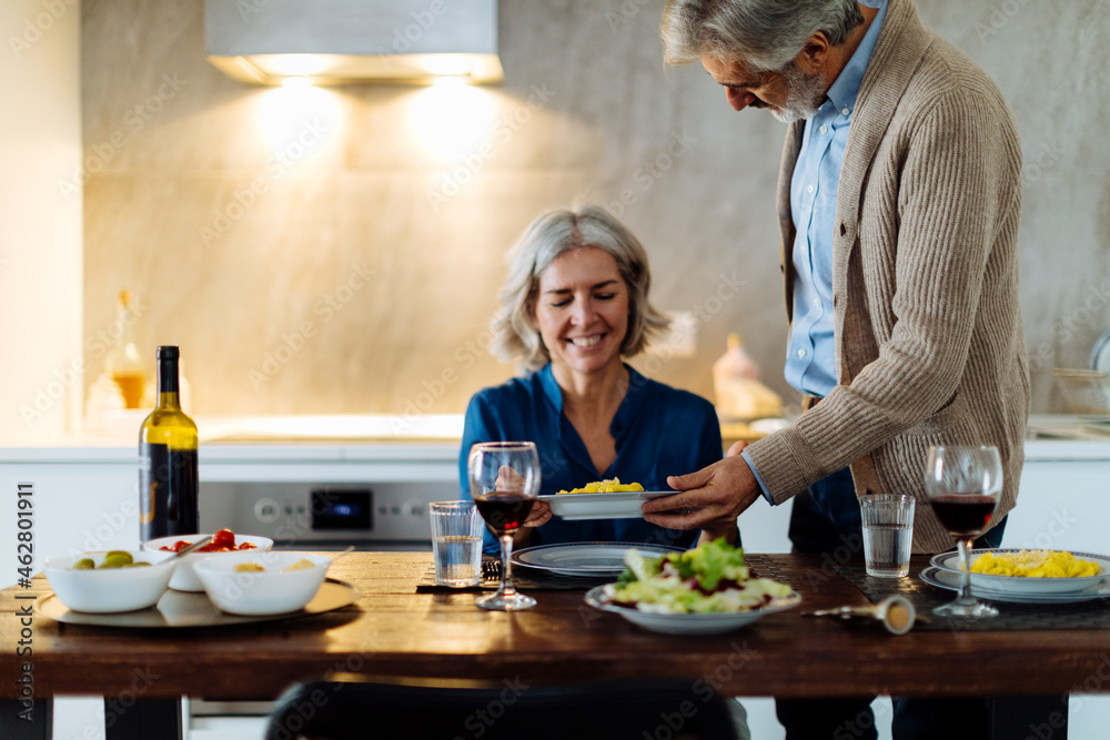 Mature man serving dinner to his wife in kitchen at home Mature man serving dinner to his wife in kitchen at home
