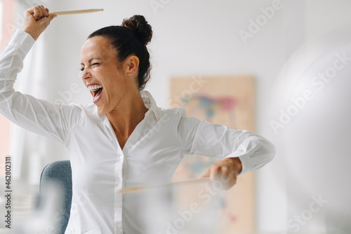 Cheerful businesswoman holding drumsticks screaming while sitting in home office photo