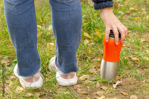 Steel thermos cup with hot drink standing on the grass