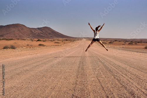 Woman jumping in the middle of a dirt road, Damaraland, Namibia
