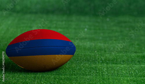 American football ball with Armenia flag on green grass background, close up